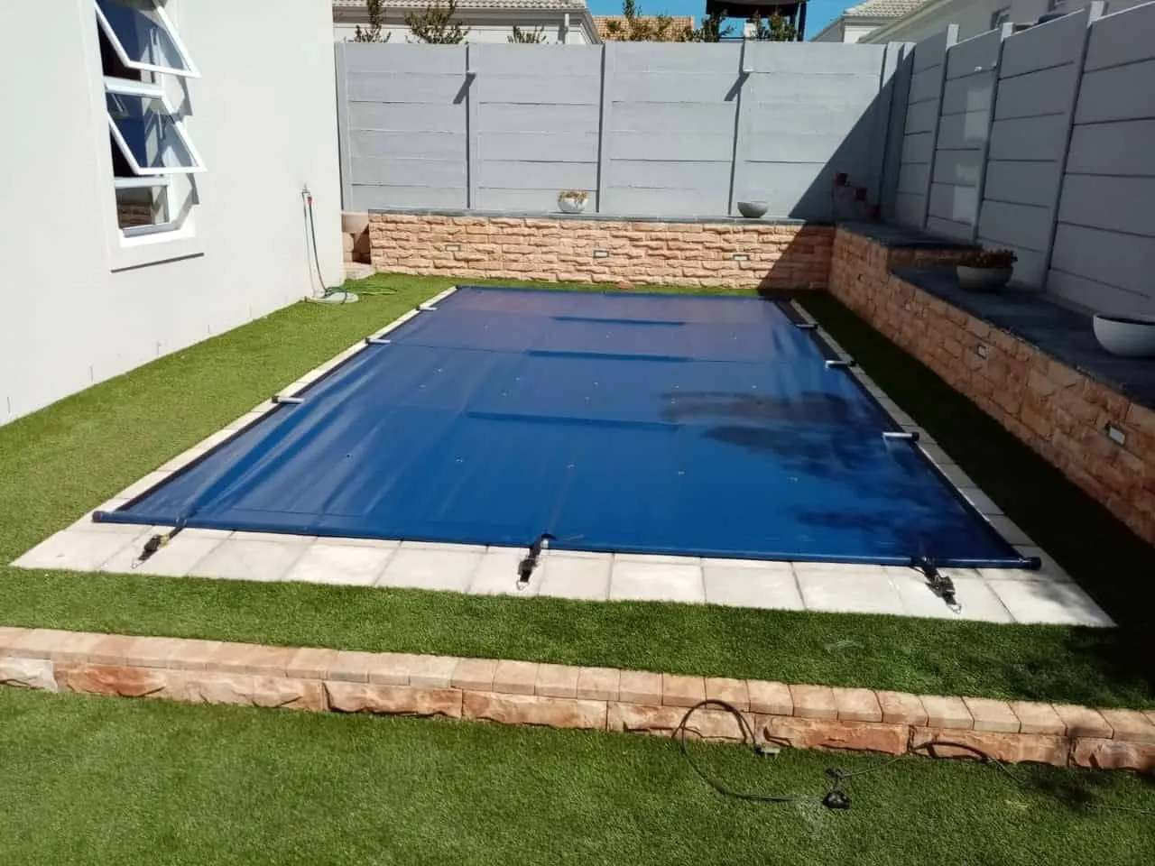 Blue safety cover installed on a pool with artificial grass